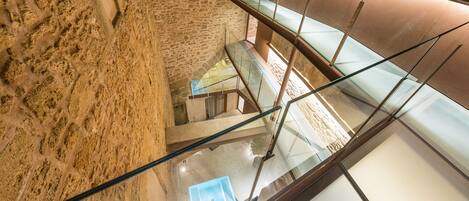 A multi-level interior with stone walls, glass railings, and a modern staircase.