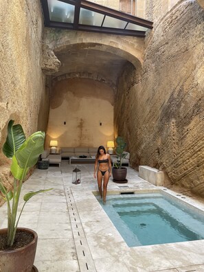 A stone-walled indoor pool area with a person walking towards the pool, surrounded by potted plants and a sofa. - Bordoy Mostatxins - Hotel Boutique Adults Only (Alcúdia)