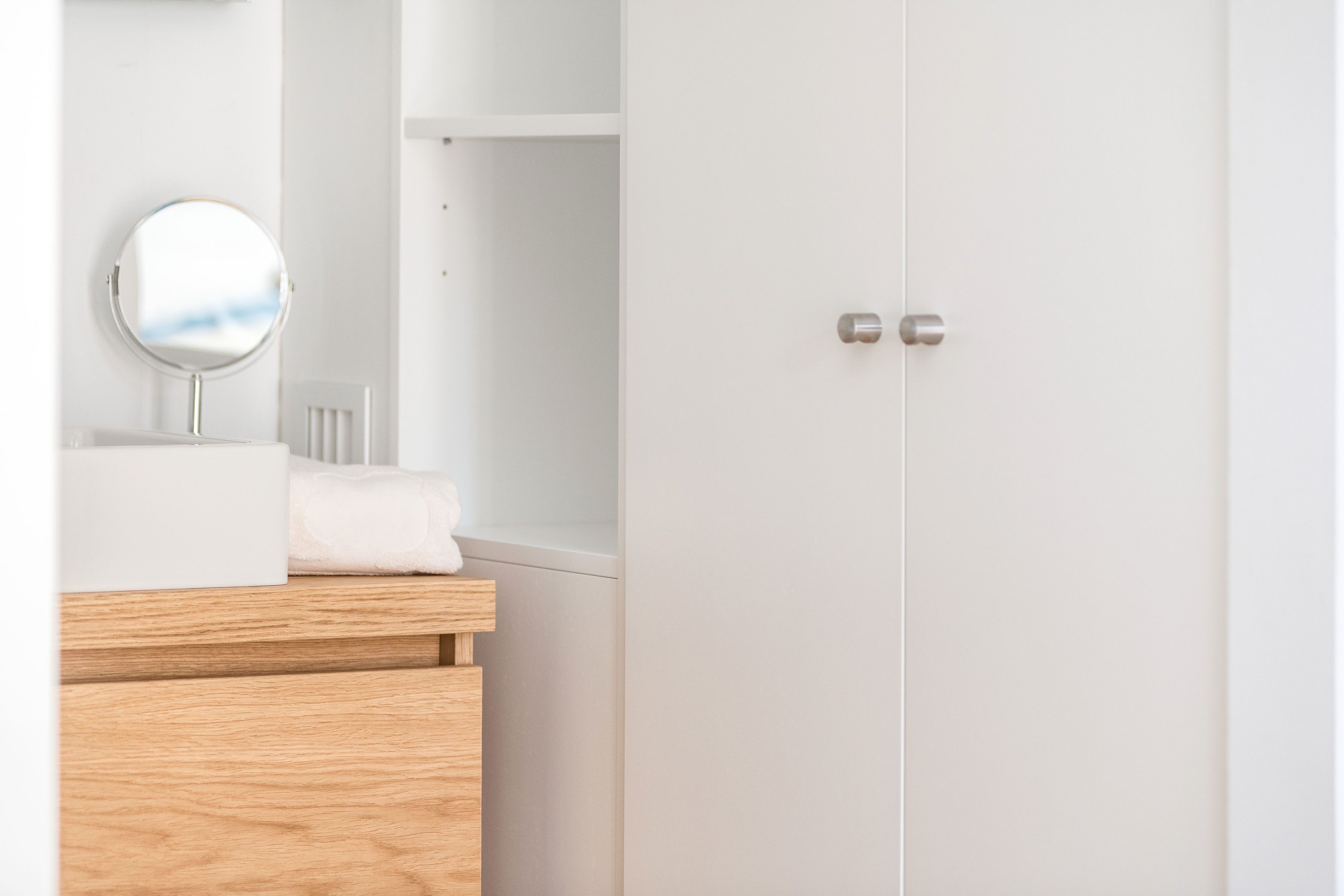 A minimalist bathroom with a wooden vanity, a round mirror, and a white door.
