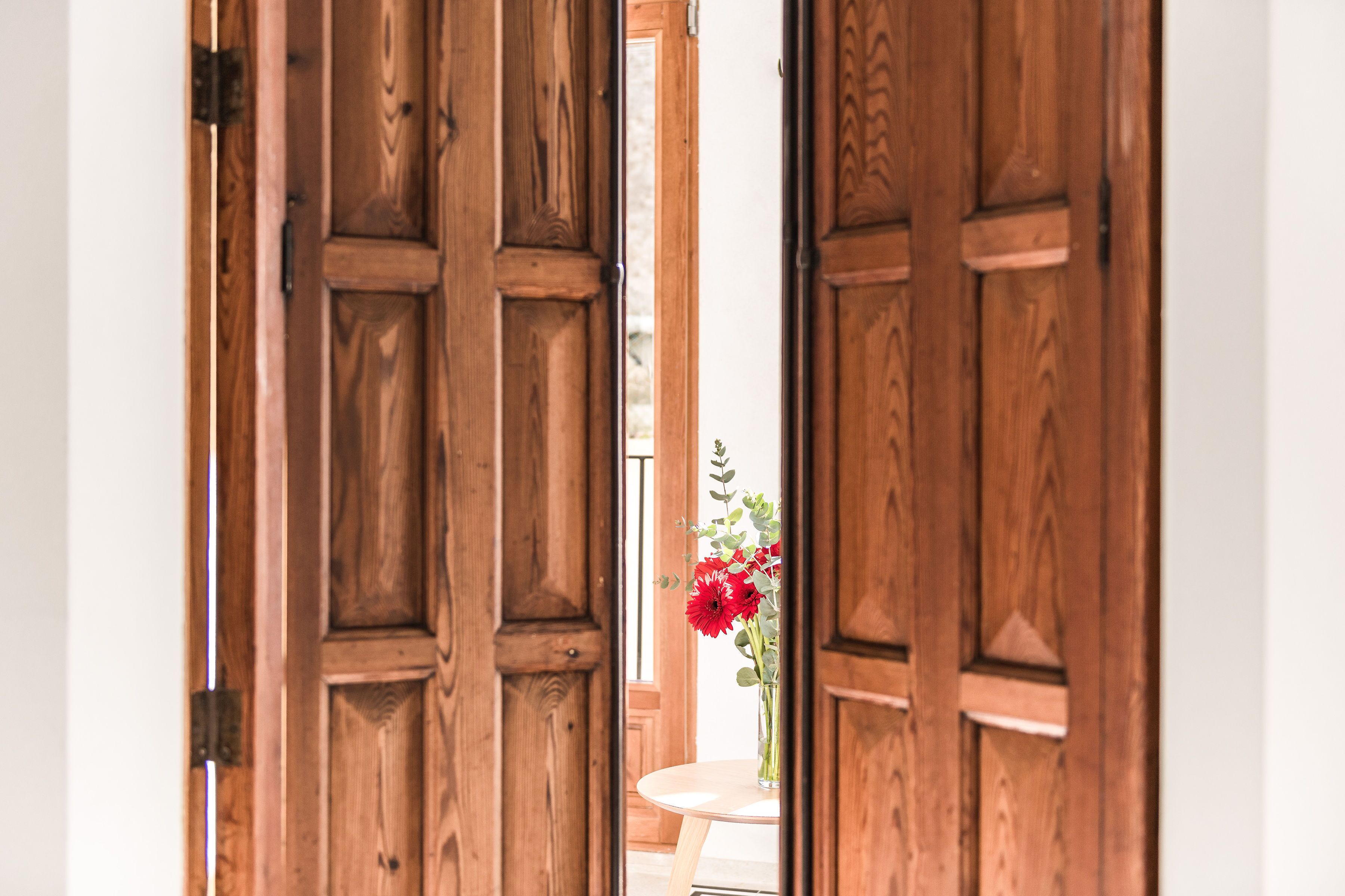 A wooden door with a glass panel, through which a table with a vase of red flowers is visible.