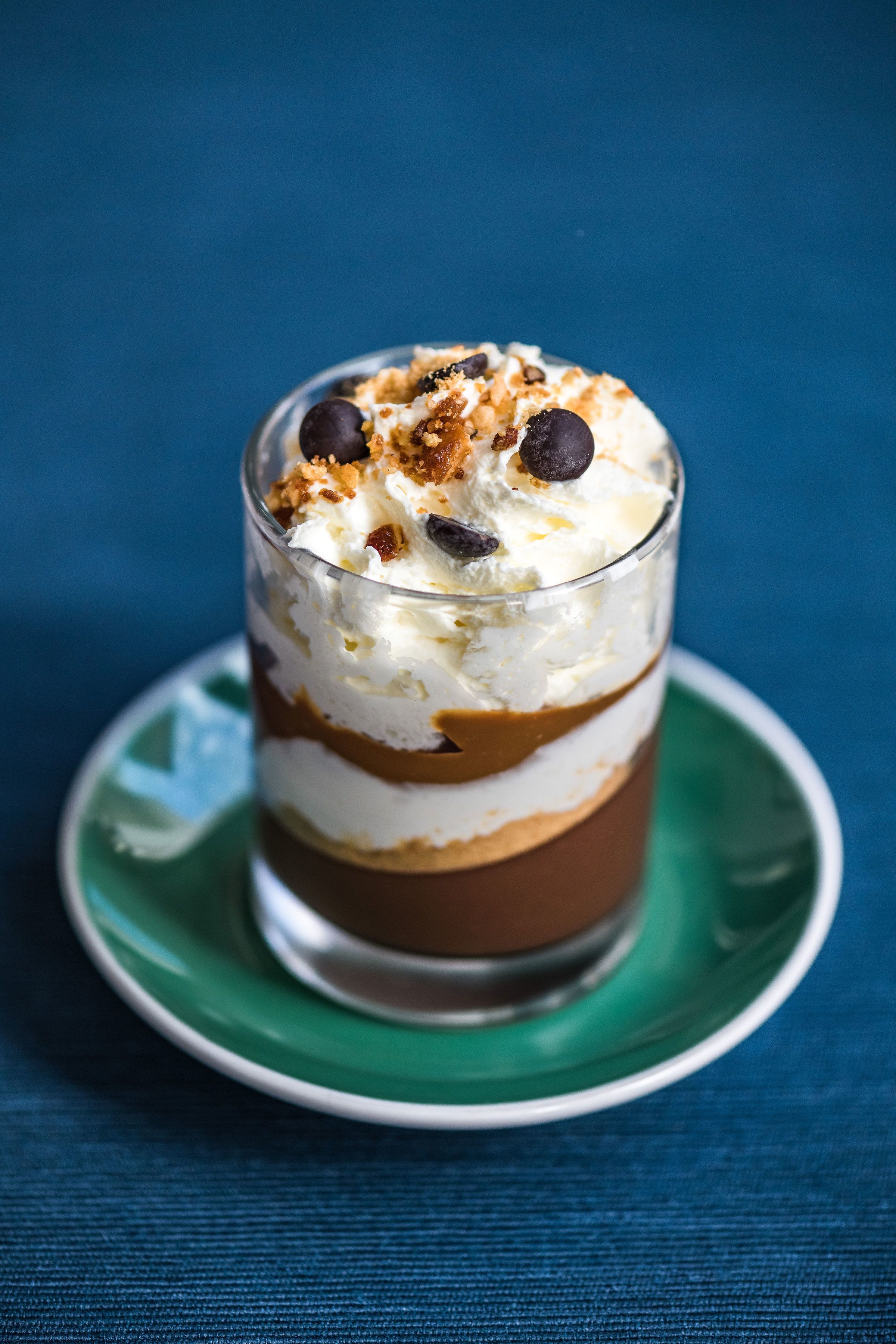 Un postre en capas en un vaso transparente sobre un plato verde.