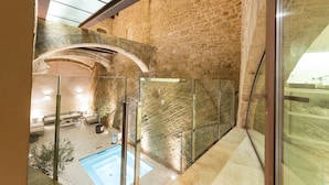 Un interior moderno con una pared de piedra, barandilla de vidrio y un área de descanso con piscina.