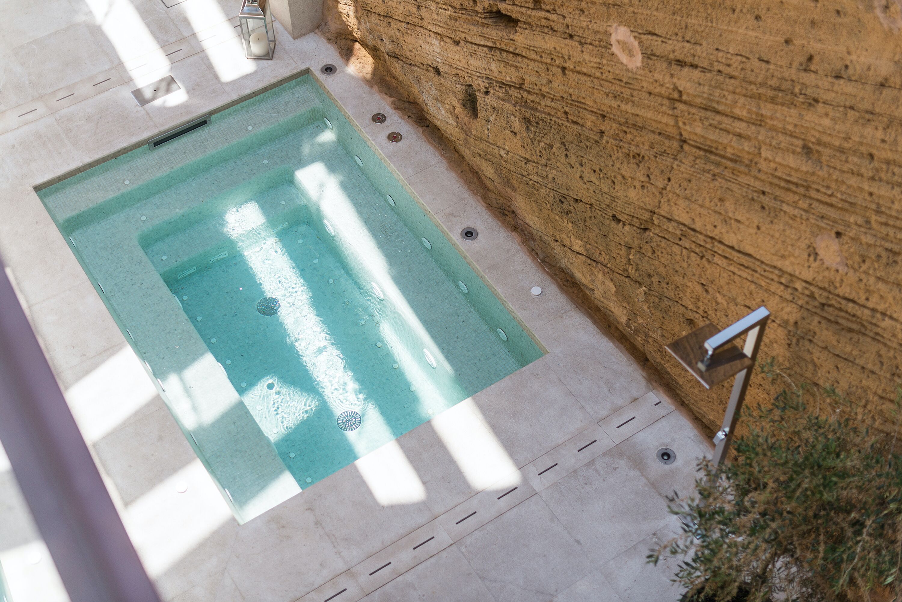 Una piscina petita i rectangular, amb vora de rajola i un desguàs, al costat d'una paret de pedra.