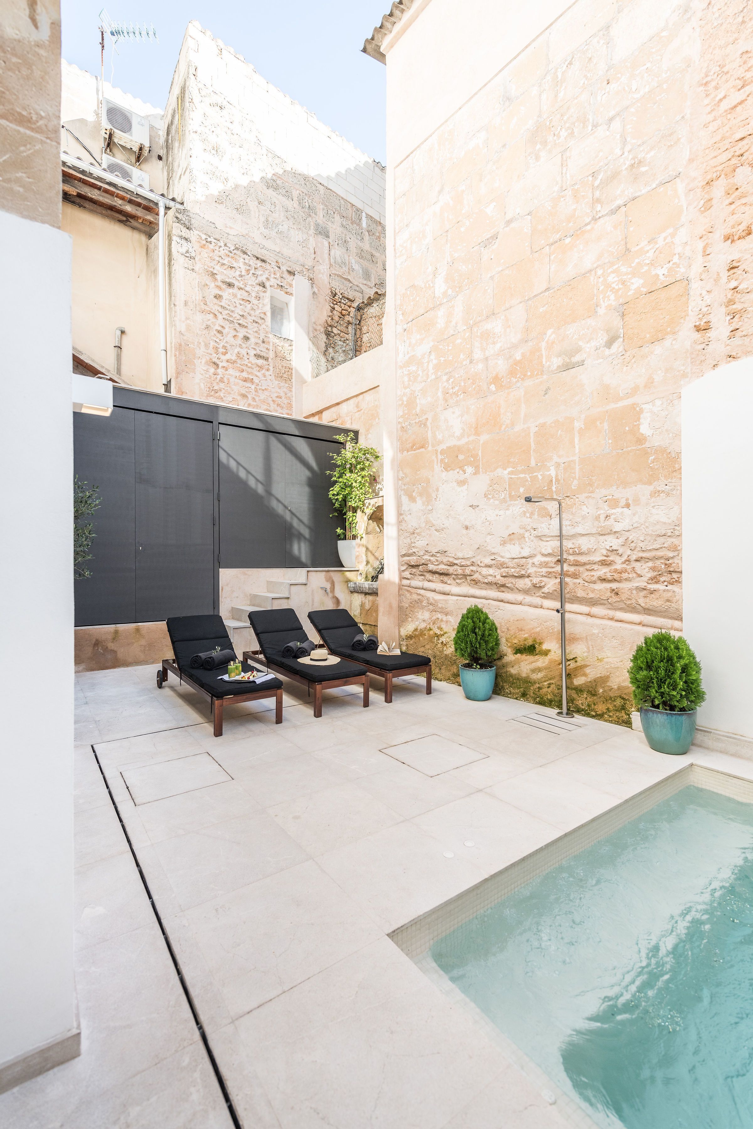 Zona de piscina con tres tumbonas, una piscina y un muro de piedra.