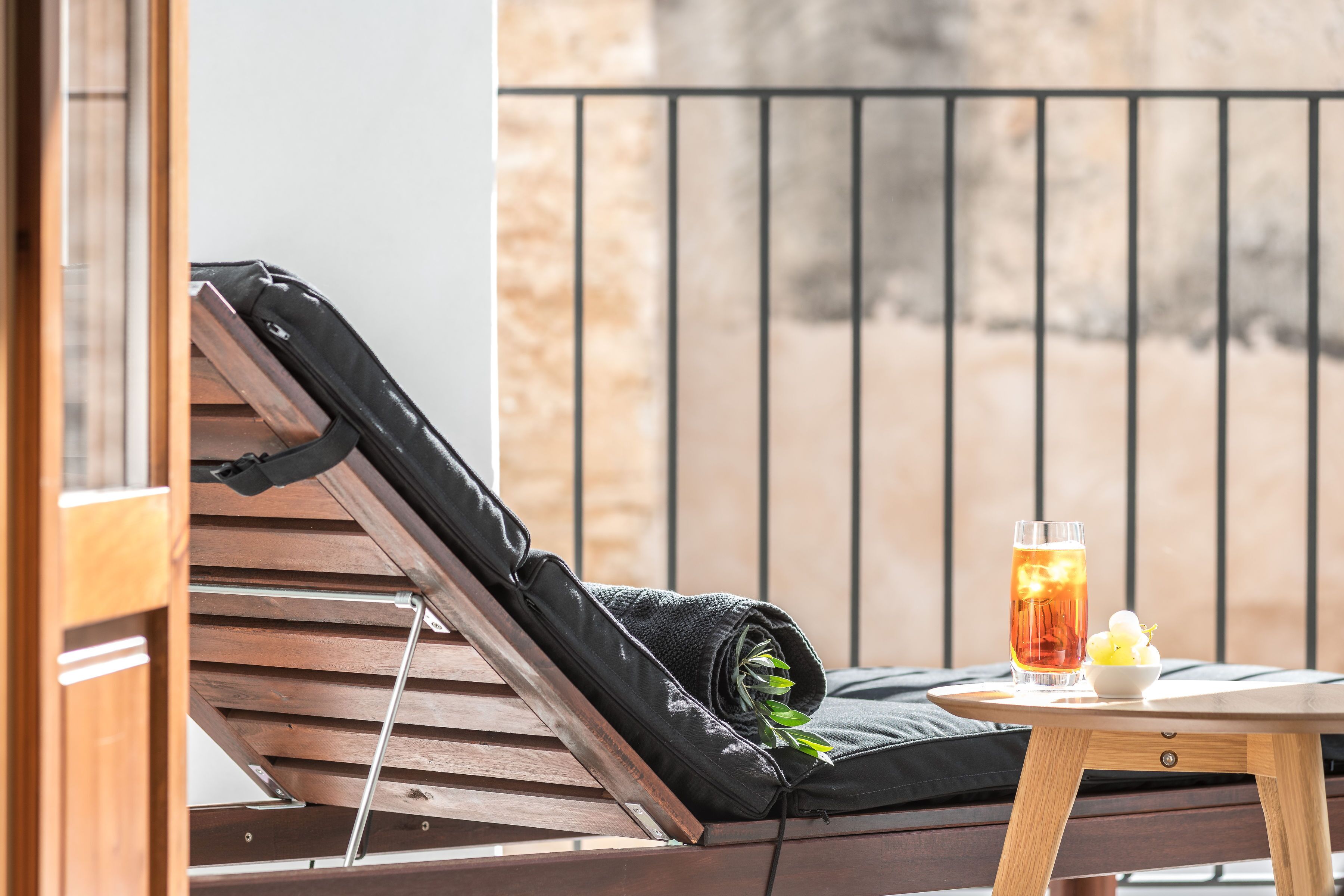 A wooden lounge chair with a black bag and a glass of iced tea on a small table.