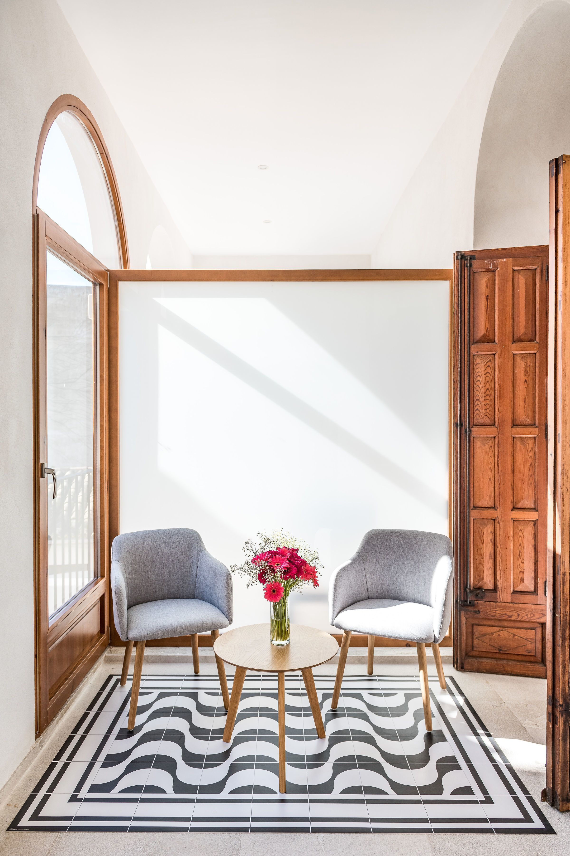 Una habitación con dos sillas, una mesita y un florero.