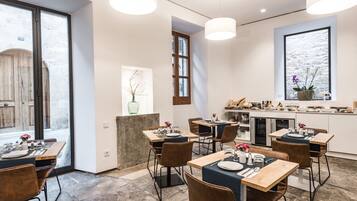 Un comedor moderno con varias mesas y sillas, una cocina al fondo y un amplio ventanal con vistas.
