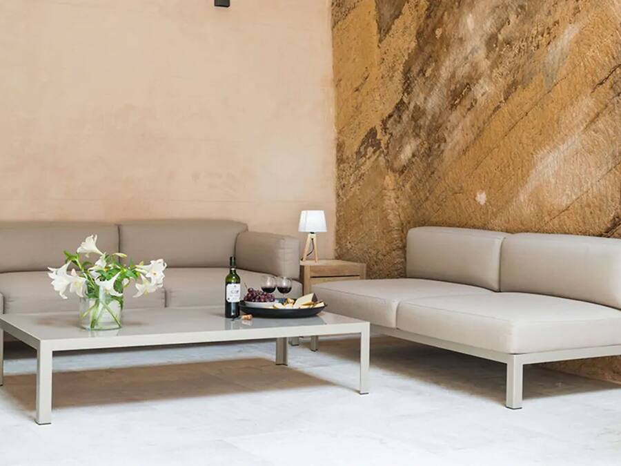 Una sala de estar moderna con un sofá color beige, una mesa de centro blanca y una pared de mármol.