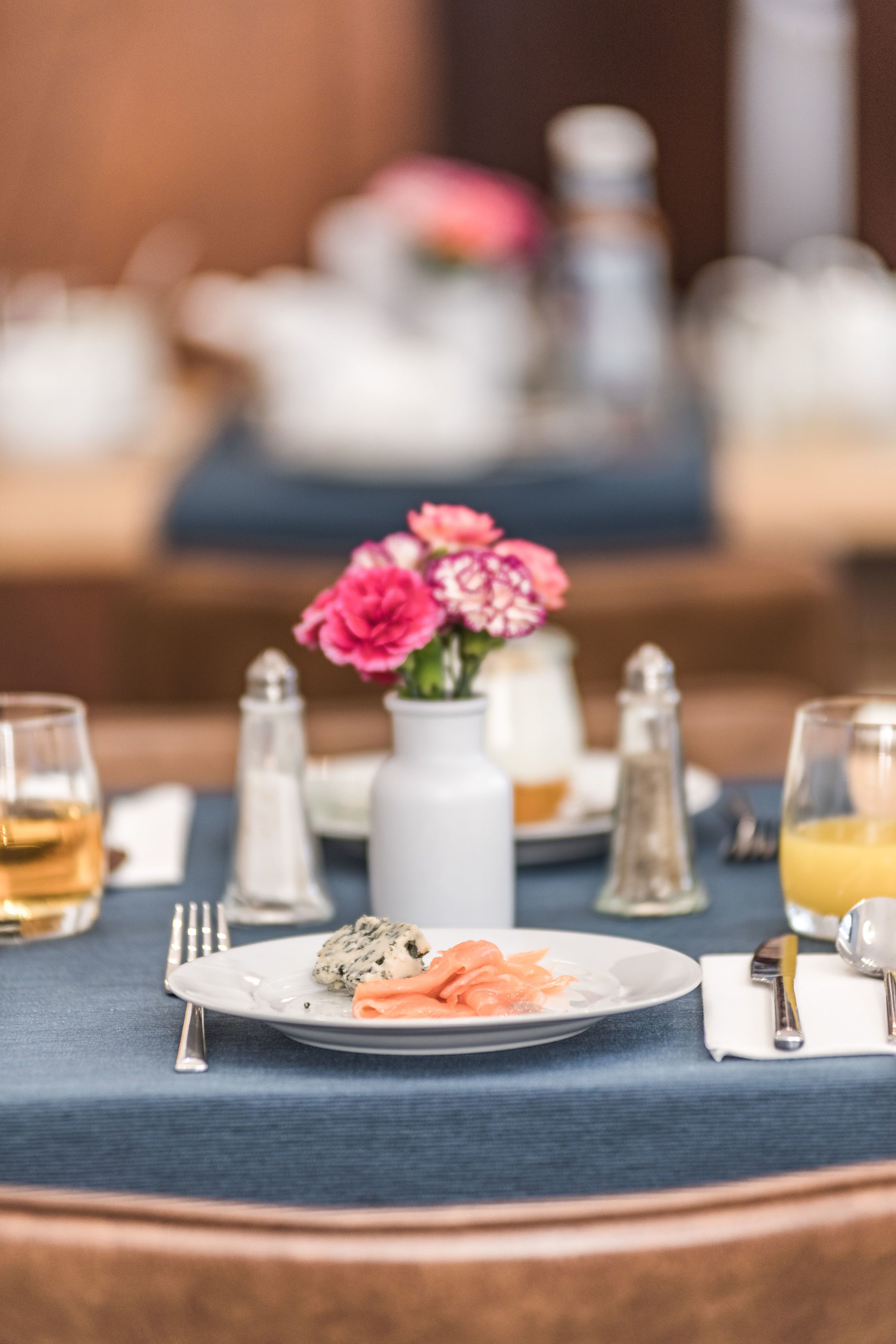 Una mesa de comedor lista con platos de comida, saleros, pimenteros, un florero con flores y vasos.