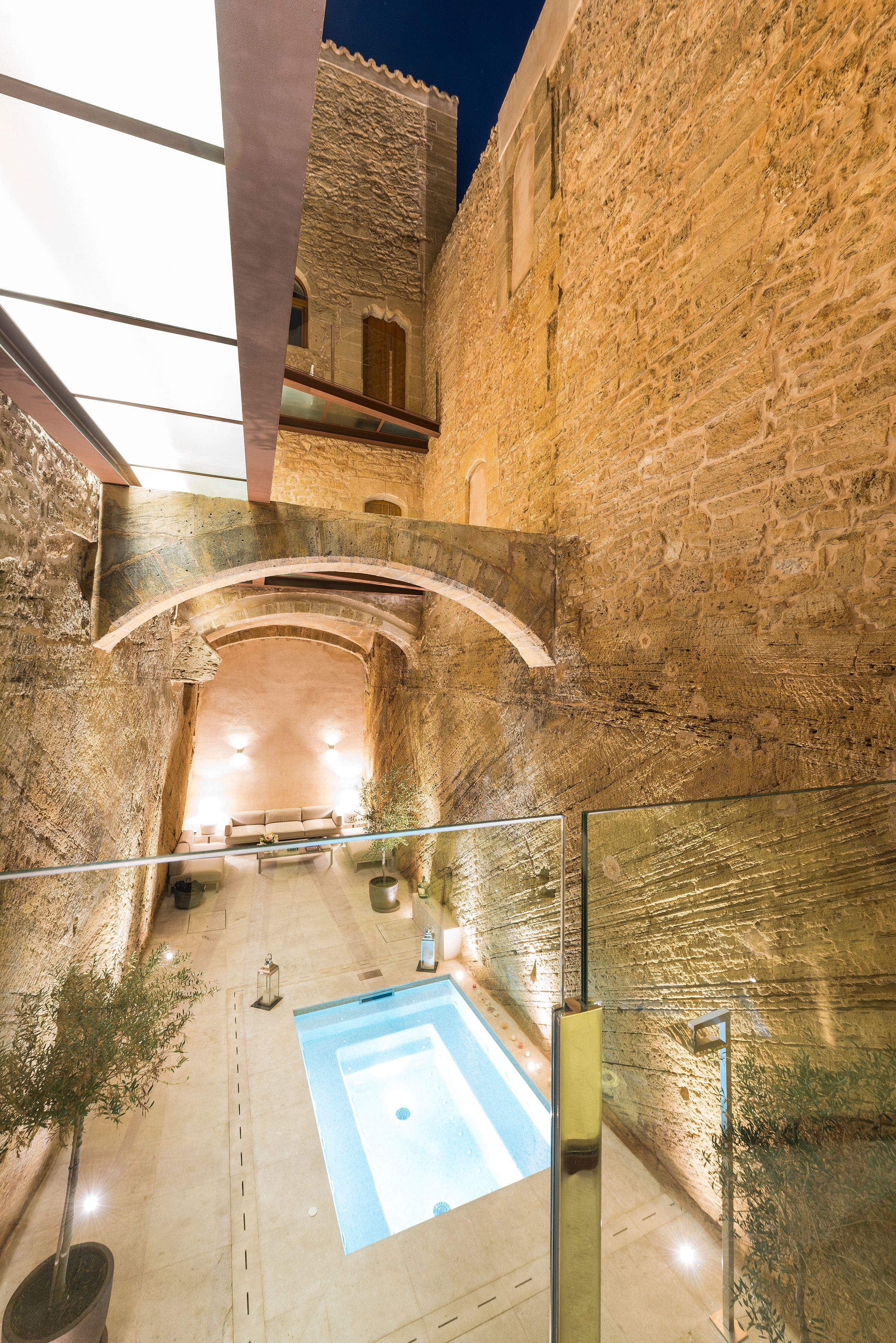 A stone-walled courtyard with a pool, a glass railing, and a bench.