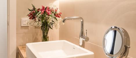 Un bagno moderno con un lavandino bianco, uno specchio e un vaso di fiori.