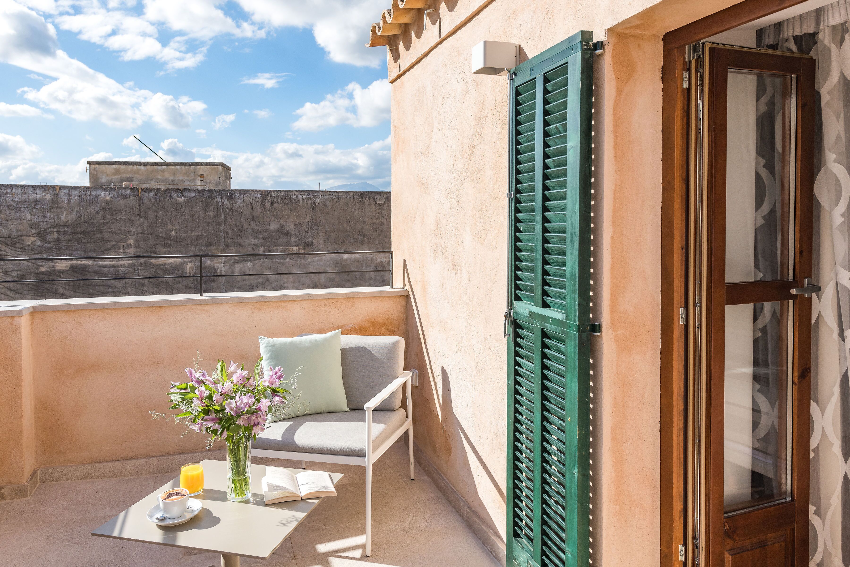 A balcony with a sofa, a table with a book and a glass of orange juice, and a vase of flowers.