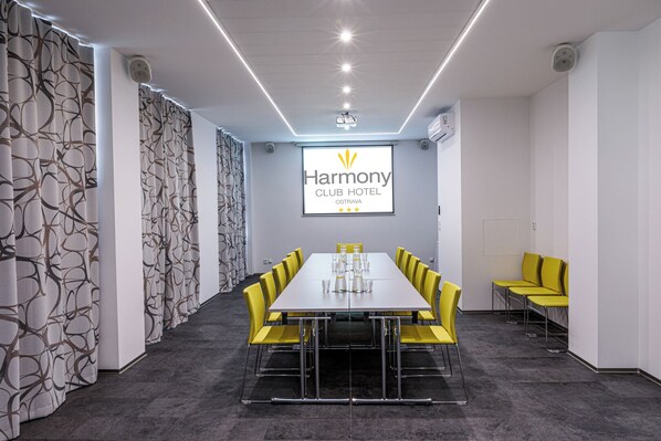 Un salón de conferencias con una larga mesa, sillas amarillas y una pantalla que muestra el logotipo del Hotel Harmony Club.