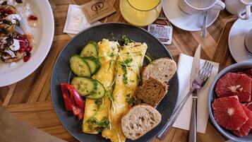 A breakfast plate with eggs, cucumber, red peppers, and bread on a wooden table.
