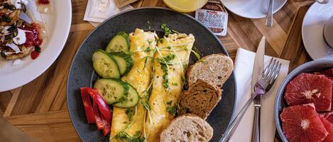 A breakfast plate with eggs, cucumber, red peppers, and bread on a wooden table.