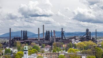Zona industrial con varias chimeneas altas y estructuras, rodeada de edificios residenciales y vegetación.