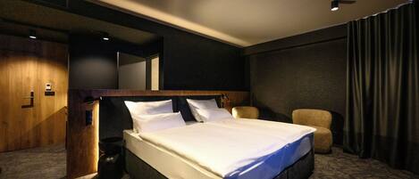Una habitación de hotel con una cama grande, un armario de madera, un sillón pequeño y un espejo en la pared.