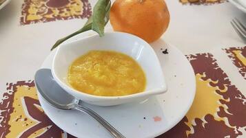 Eine Schüssel Suppe auf einem weißen Teller, eine ganze Orange und ein grünes Blatt auf dem Tisch.