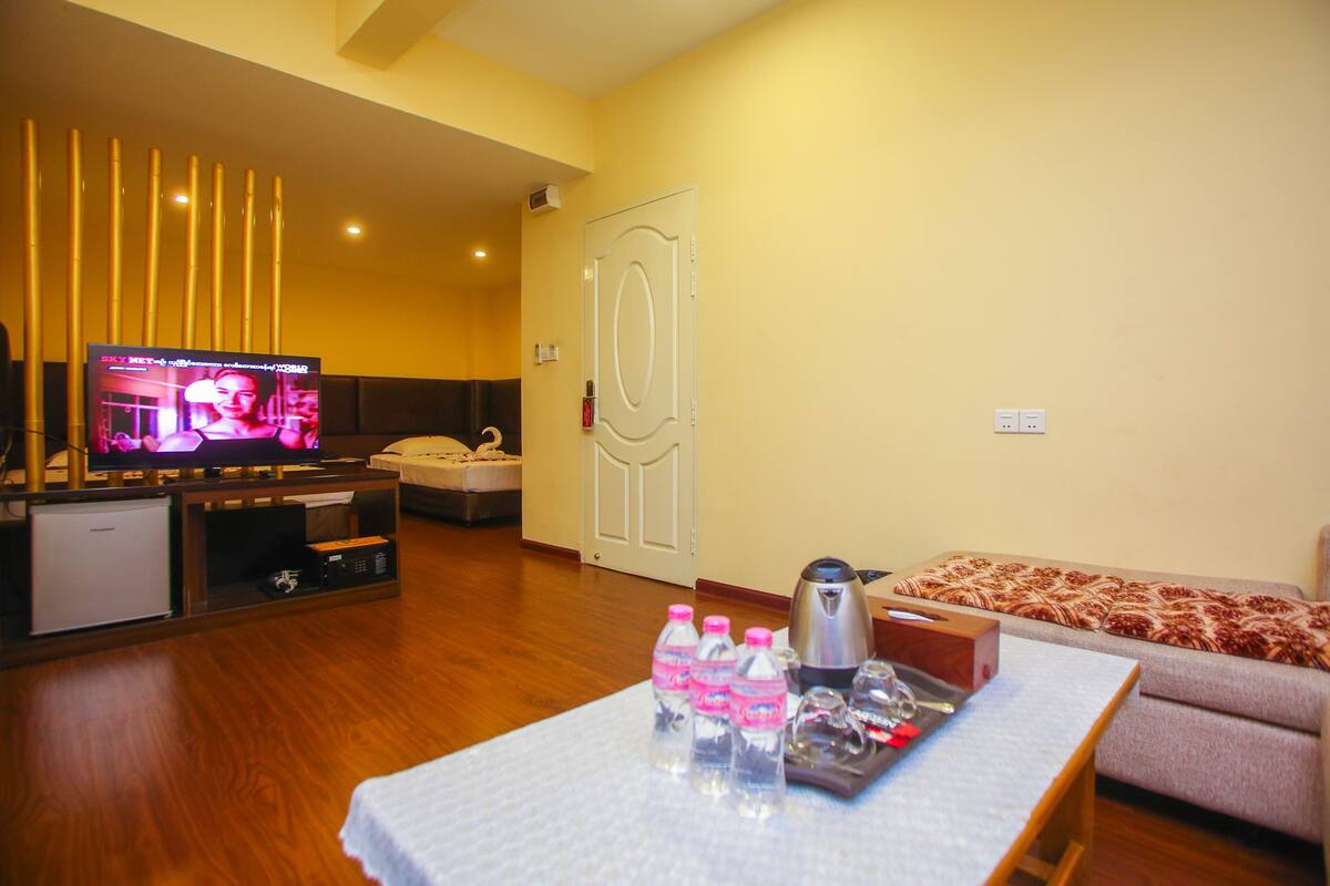 A living room with a television, a sofa, a coffee table with water bottles, and a small refrigerator.