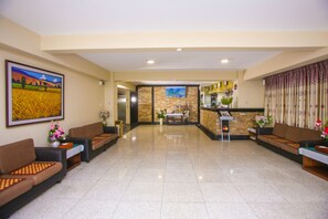 A hotel lobby with a reception desk, seating area, and a large painting on the wall.