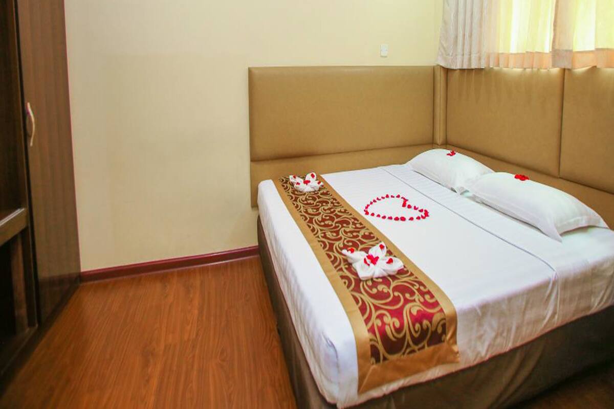 A hotel room with a bed, wooden wardrobe, and a window with curtains.