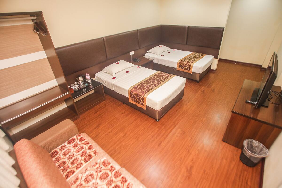 A hotel room with two beds, a small table, a TV, and a trash bin.