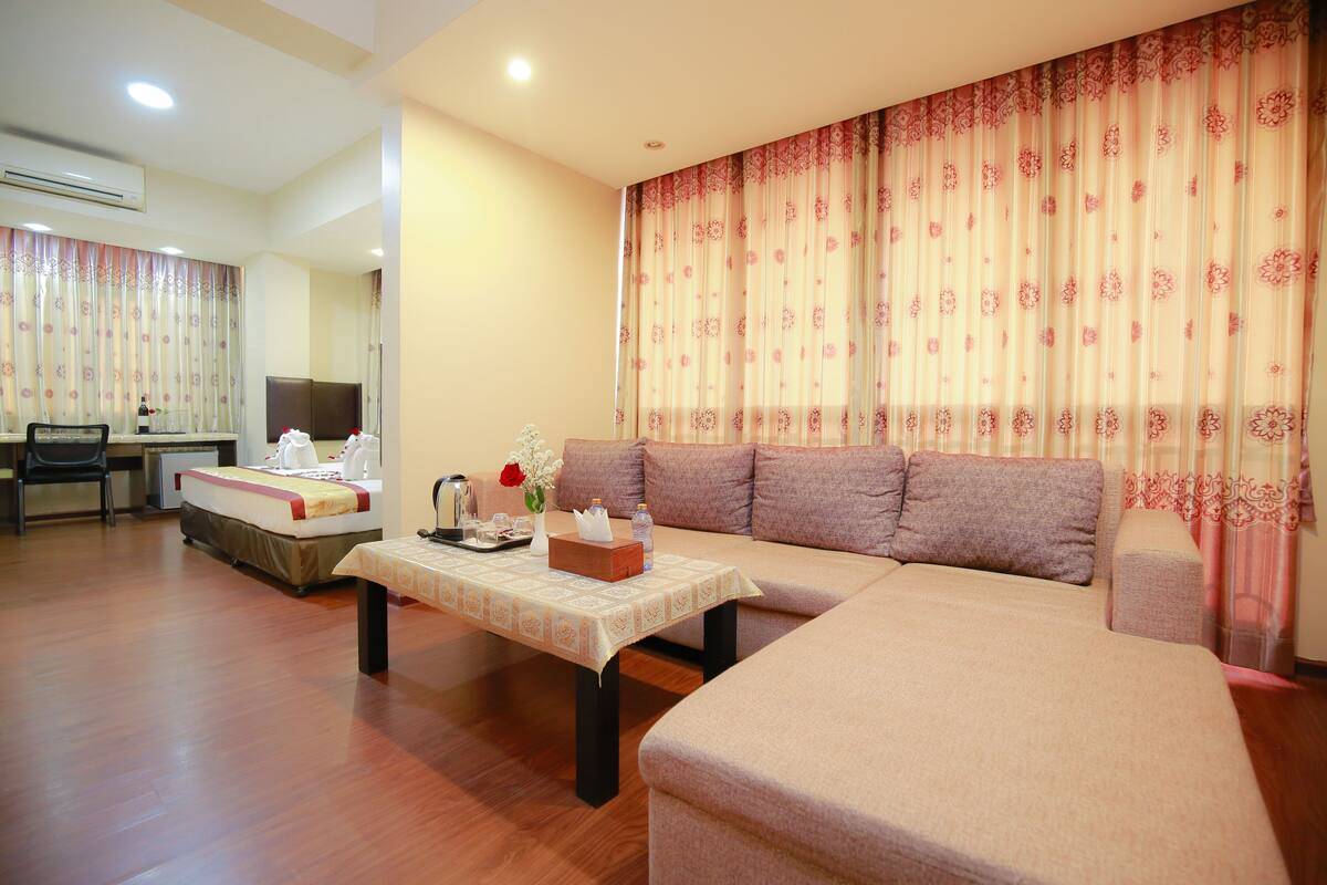 A hotel room with a sofa, a dining table, a TV, and a desk.