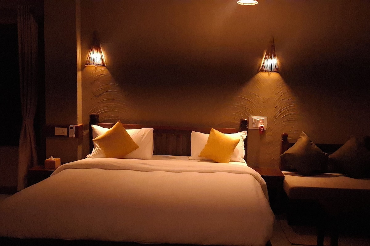 A hotel room with a large bed, two bedside lamps, and a nightstand with a phone and a box.