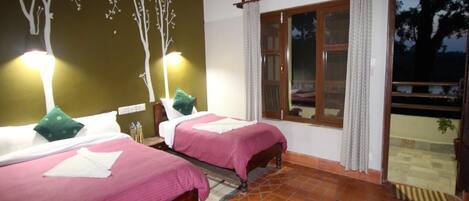 Una habitación con dos camas, una ventana con cortinas, un mural de un árbol en la pared y suelo de baldosas.
