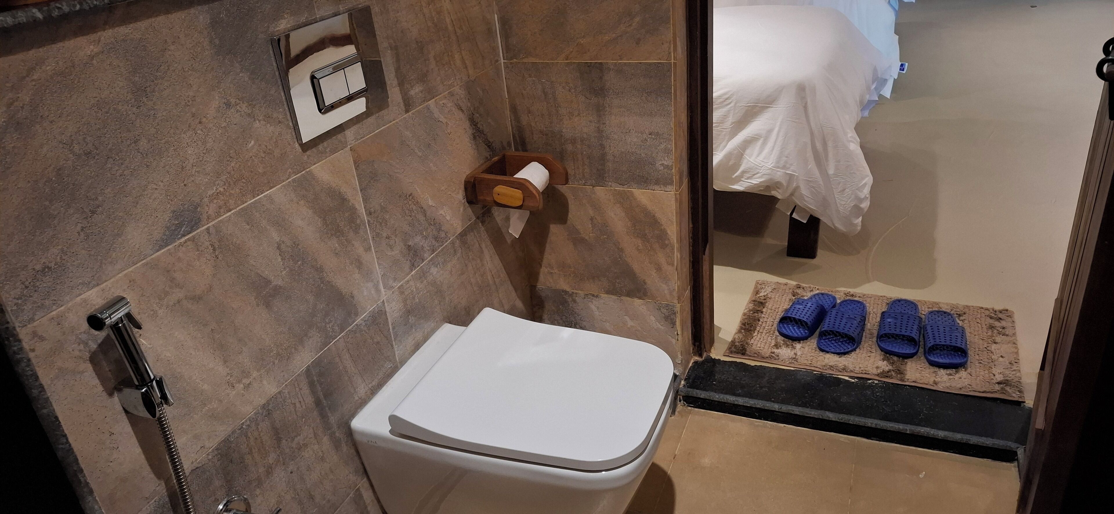 A bathroom with a toilet, shower, and a bed visible through an open door.