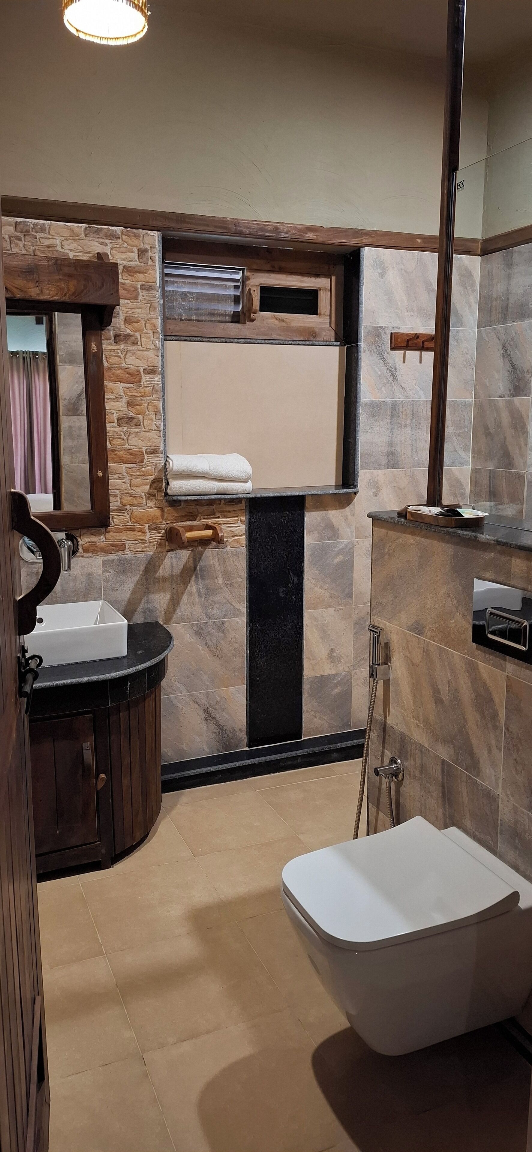 A bathroom with a stone wall, a wooden vanity, a white bathtub, and a mirror.