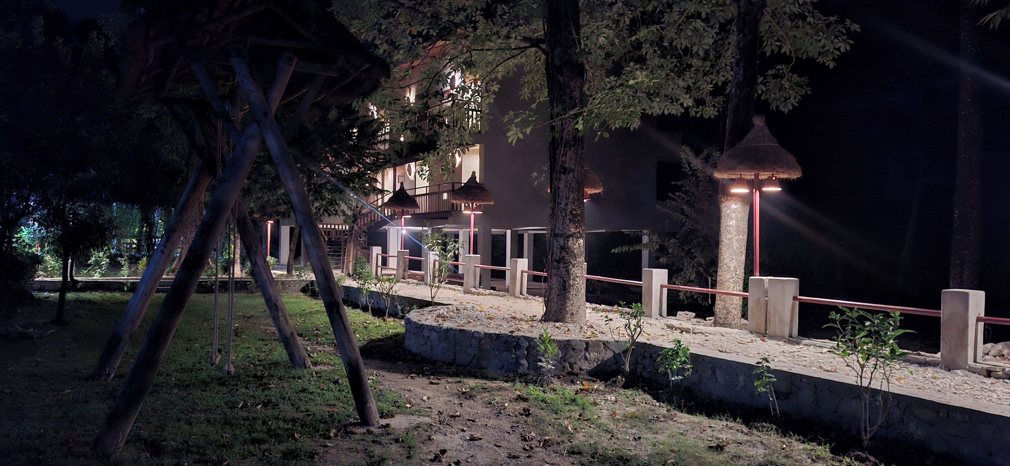 A nighttime view of a resort with a pool area, surrounded by trees and a stone pathway.