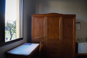 A room with a wooden wardrobe, a desk with a laptop, and a window with a view of trees. - Hotel Sorrento (Belo Horizonte)