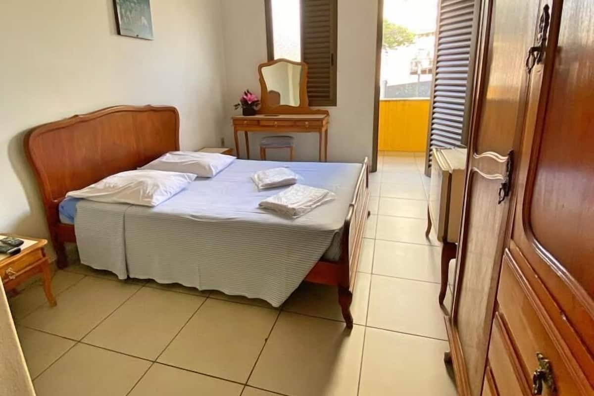 Une chambre à coucher avec un lit, une armoire en bois, un bureau avec un miroir et un ventilateur de plafond.