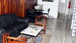 Una sala de estar con un sofá de cuero negro, una mesa de centro de madera con revistas, y una alfombra estampada.
