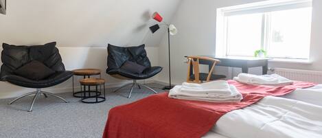 A hotel room with a bed, two chairs, a small table, a floor lamp, and a window with a view of greenery.