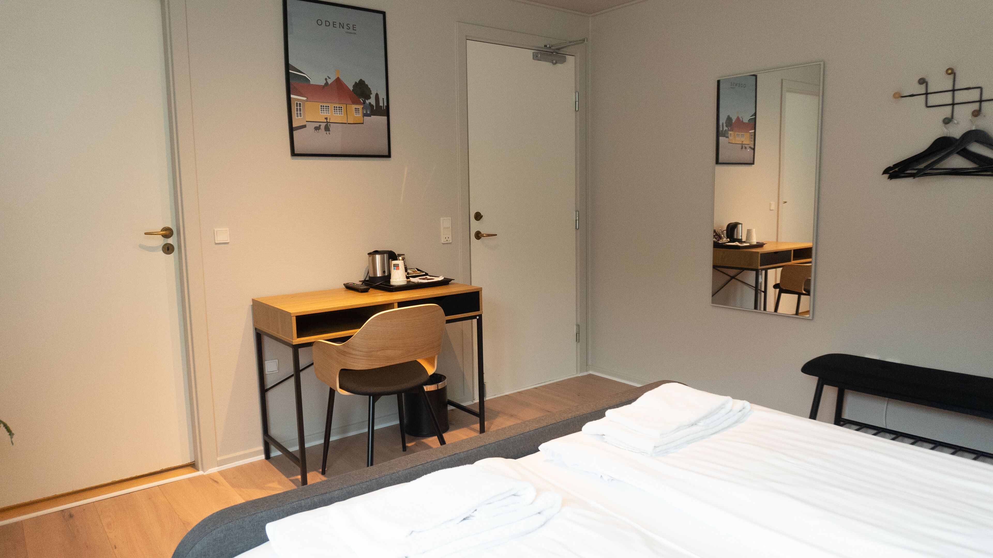Une chambre d’hôtel comprenant un lit, un bureau avec une chaise, une machine à café, un miroir et un porte-manteau.