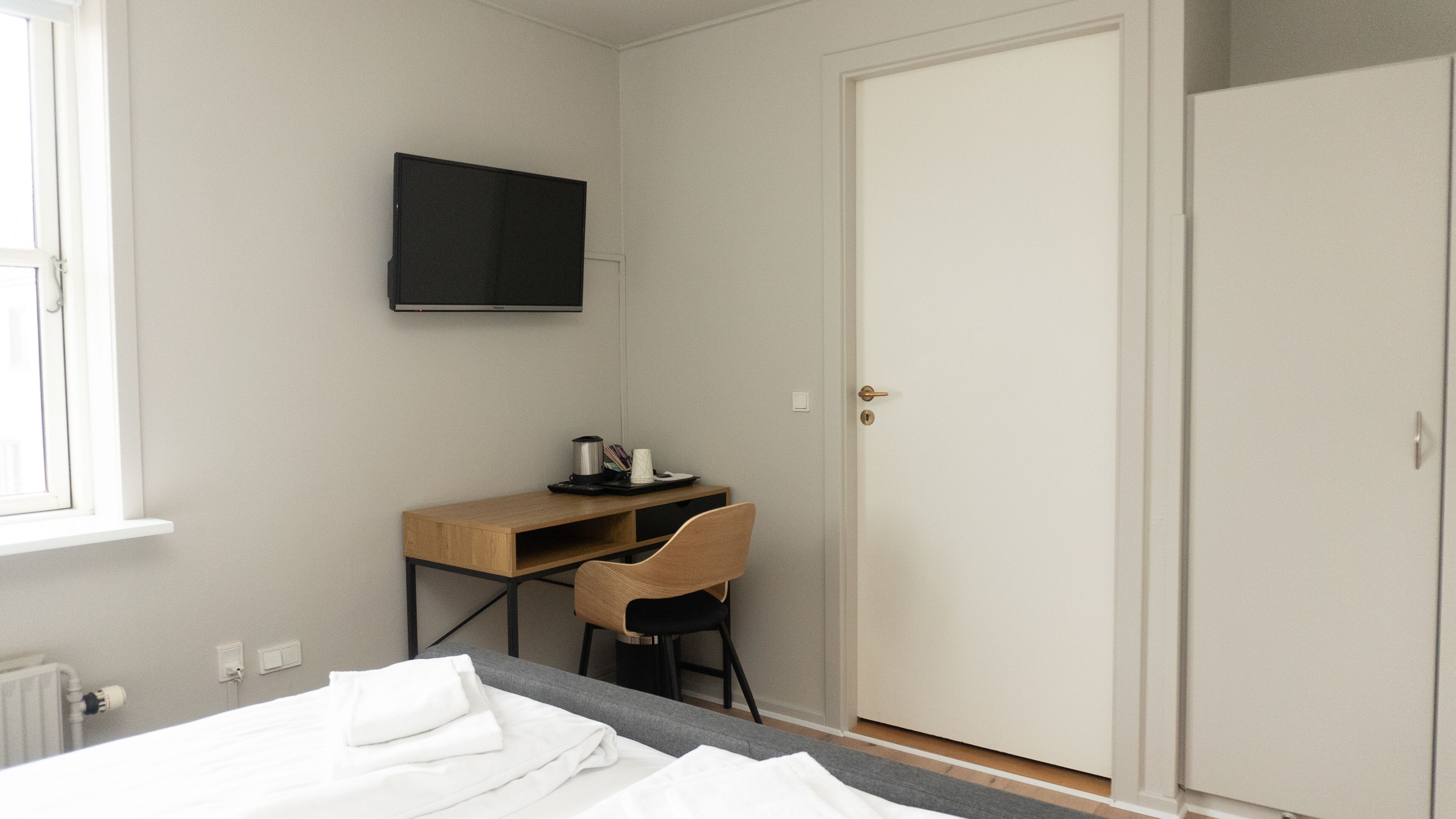 A bedroom with a bed, a desk, a chair, a television, and a wardrobe.