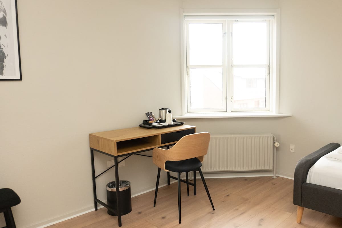 A small, neatly organized room with a wooden desk, a chair, a bed, and a radiator.