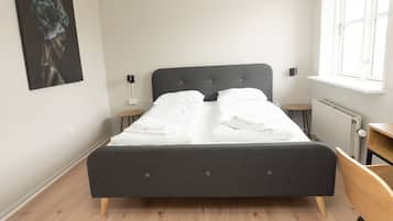 Ein ordentlich bezogenes Bett mit weißen Leinen, einem dunkelgrauen Kopfteil und zwei Nachttischen mit Lampen.