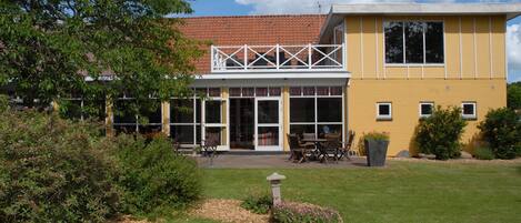 Een gebouw met twee verdiepingen, een gele gevel, grote ramen en een balkon.
