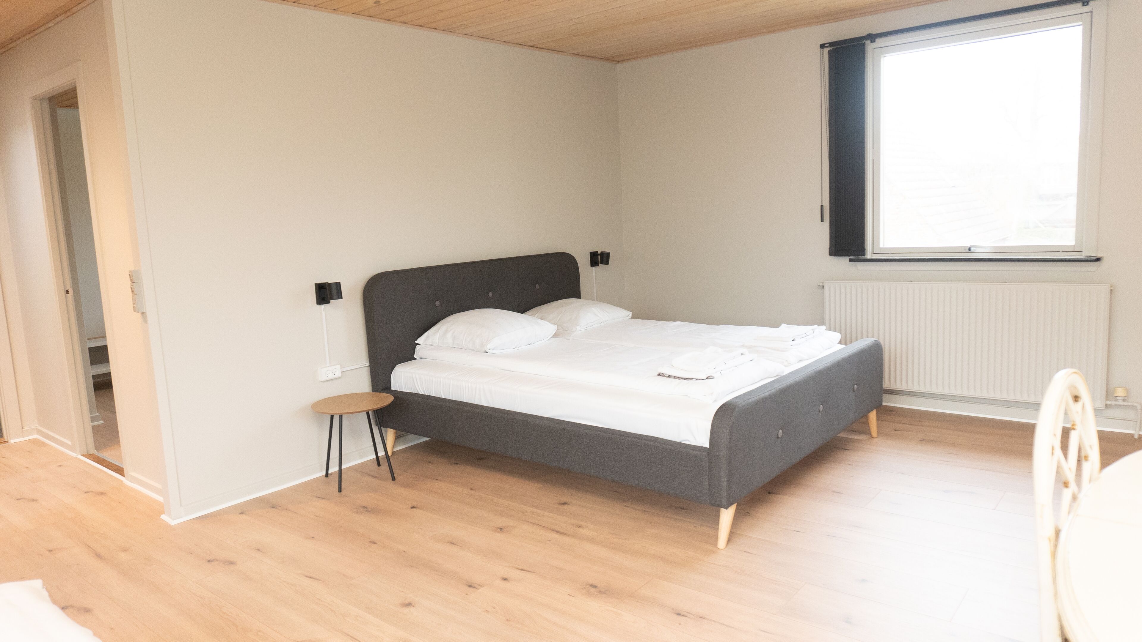 A bedroom with a bed, a small stool, a window, and a radiator.