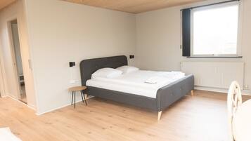 Quarto com uma cama, um banquinho, uma janela e um radiador.