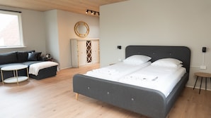 A modern bedroom with a large bed, a sofa, a small table, and a wardrobe. - Hotel Smedegaarden (Lem)