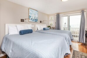 A hotel room with two beds, a balcony with curtains, and artwork on the walls.