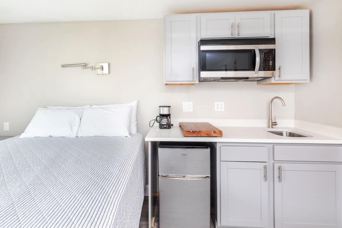 A compact hotel room with a bed, a kitchenette with a microwave, a coffee maker, and a small refrigerator.