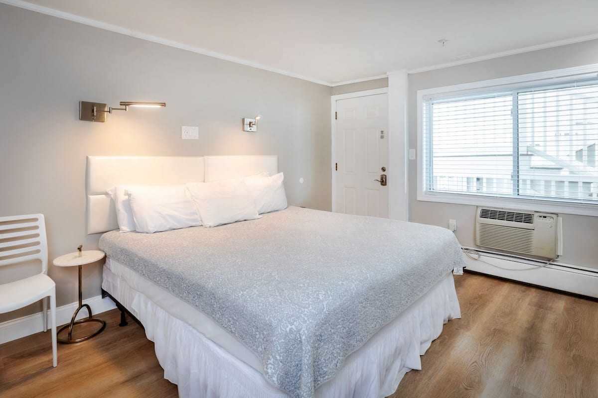 A bedroom with a bed, bedside table, chair, and a window with blinds.