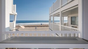 A balcony with a view of the beach, a pool area with three chairs, and a building with multiple balconies. - Atlantic Motel (Hampton)