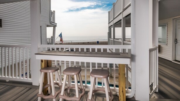 A covered outdoor area with a pool, white railings, and a view of the ocean. - Atlantic Motel (Hampton)