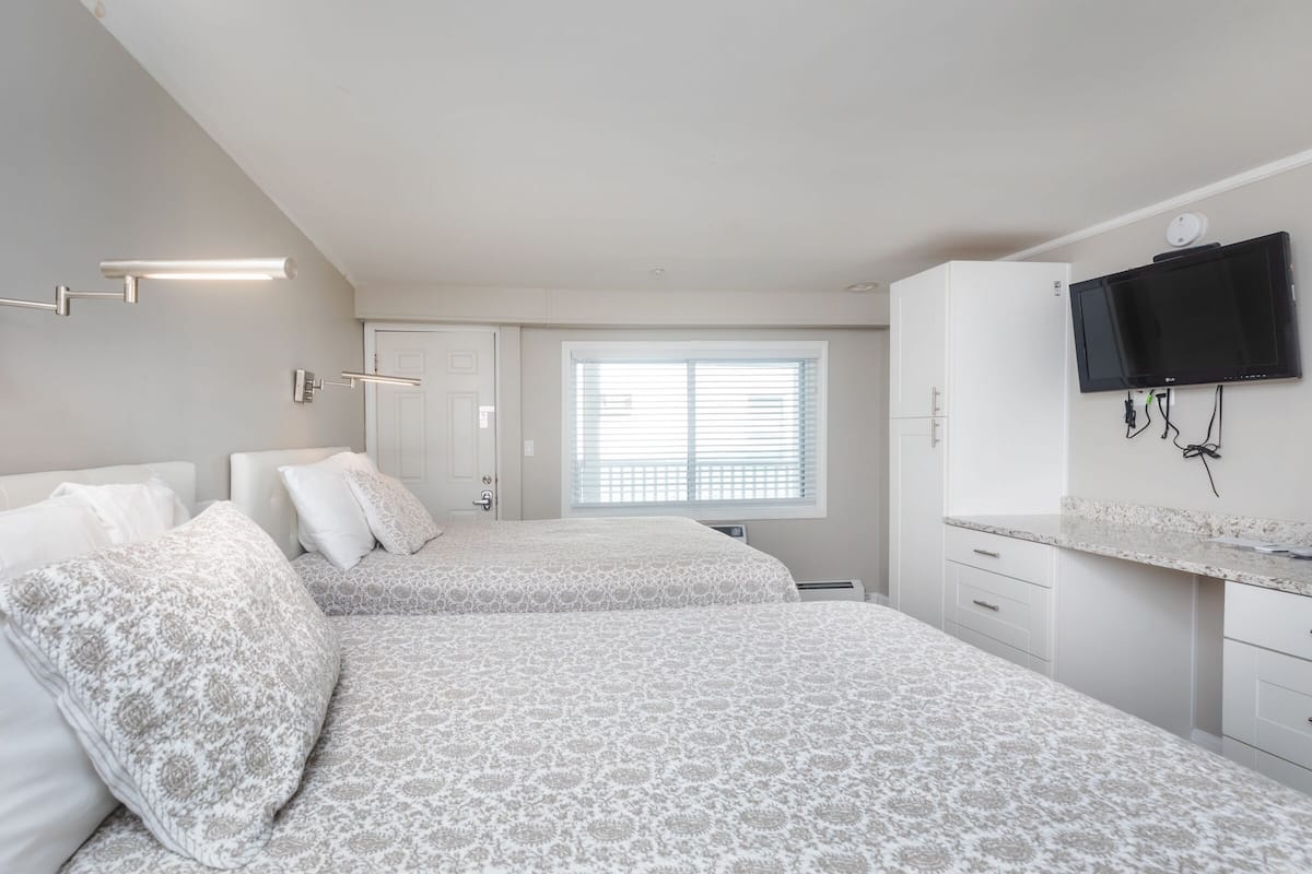 A bedroom with two beds, a TV mounted on the wall, and a window with blinds.